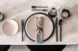 Elegantes Besteckset in Schwarz, bestehend aus Messer, Gabel und Löffel, auf einem gedeckten Tisch mit Tellern und Gläsern, aus der Vogelperspektive fotografiert.