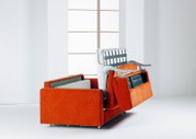 Orangefarbenes Schlafsofa mit ausgeklappter Bettmechanik, schräg von vorne in einem hellen Wohnraum gezeigt