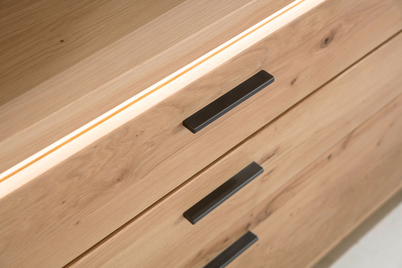 Nahaufnahme eines Sideboards aus Holz mit drei Schubladen und schwarzen Griffen, Perspektive von oben.