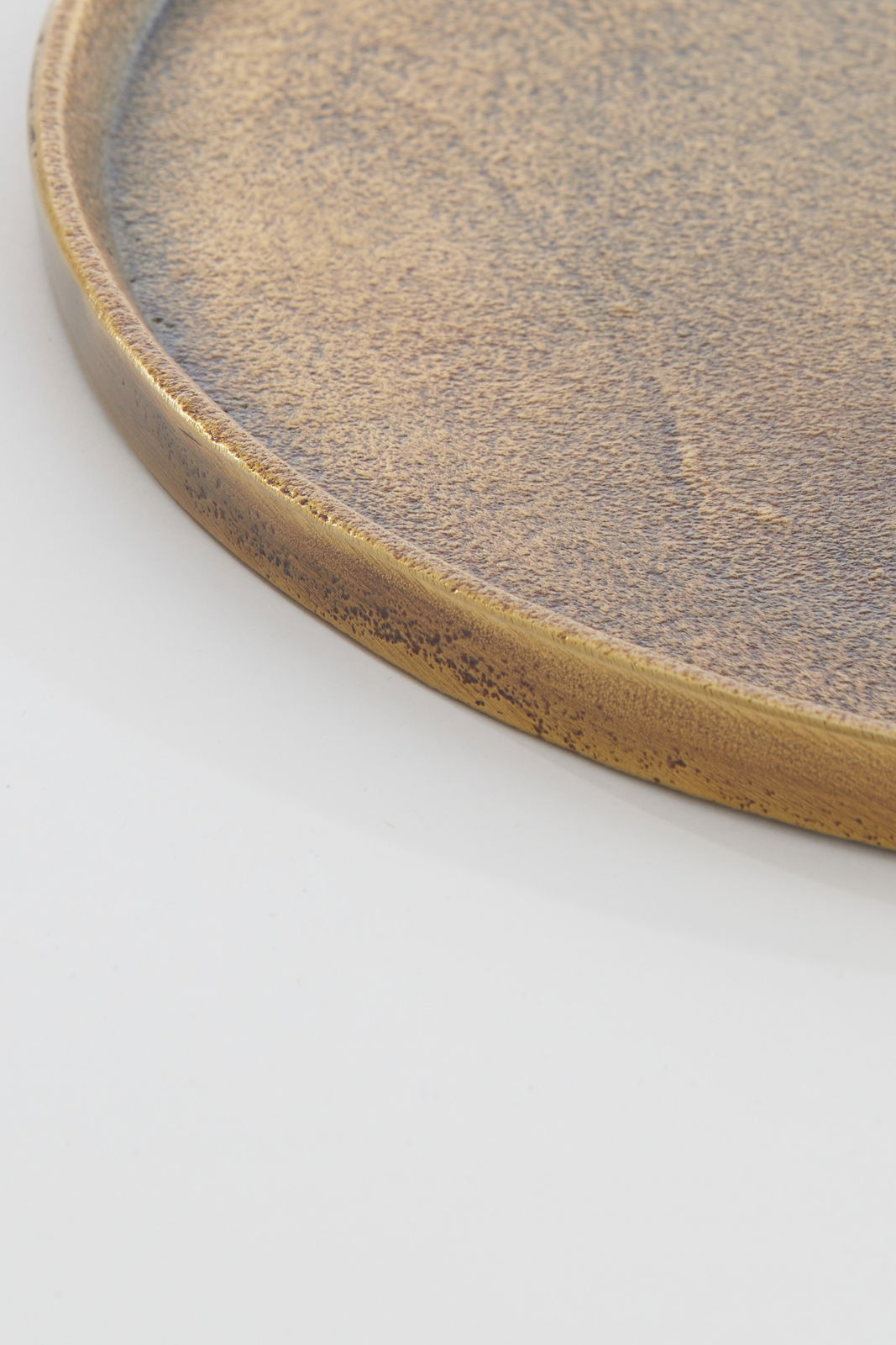 Nahaufnahme einer runden, flachen Schale mit antiker, goldener Patina, seitliche Perspektive.