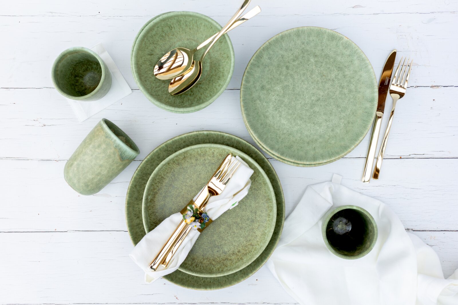 Gipfelstück Schüssel 4er-Set MOOS´N´STEIN Draufsicht auf ein gedecktes Tisch-Arrangement mit grün glasiertem Keramikgeschirr (Teller, Schalen, Becher) und goldfarbenem Besteck auf weißem Holztisch.