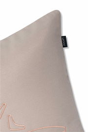 Nahaufnahme einer beigen Zierkissenhülle mit dezentem Stickmuster und einem kleinen schwarzen Etikett an der Seite.