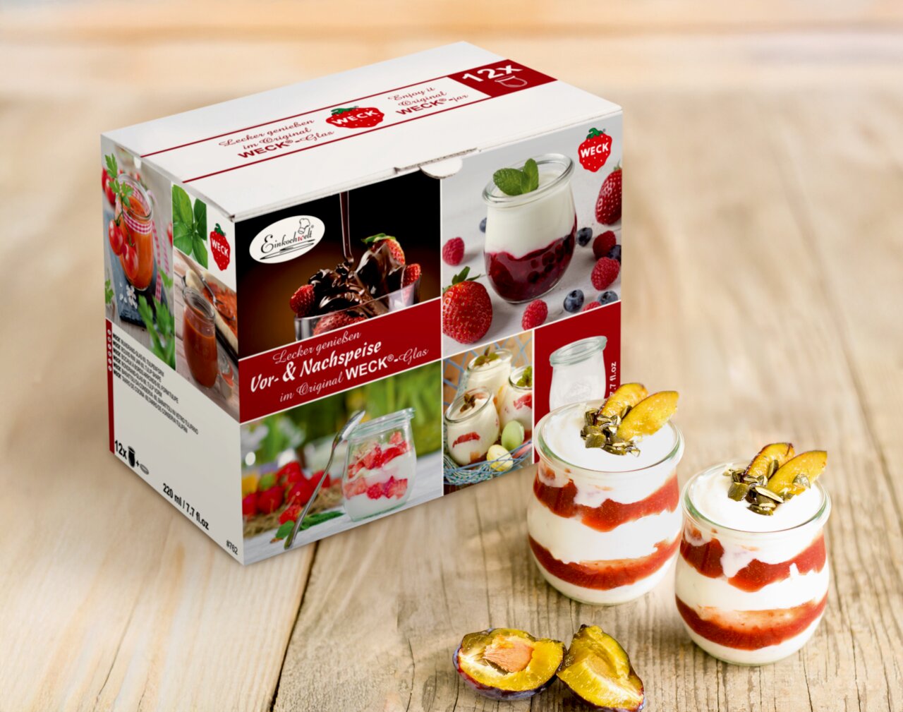 Verpackung und zwei gefüllte Vor- & Nachspeisengläser, frontal fotografiert, mit Schichtdessert und Pflaumen dekoriert.