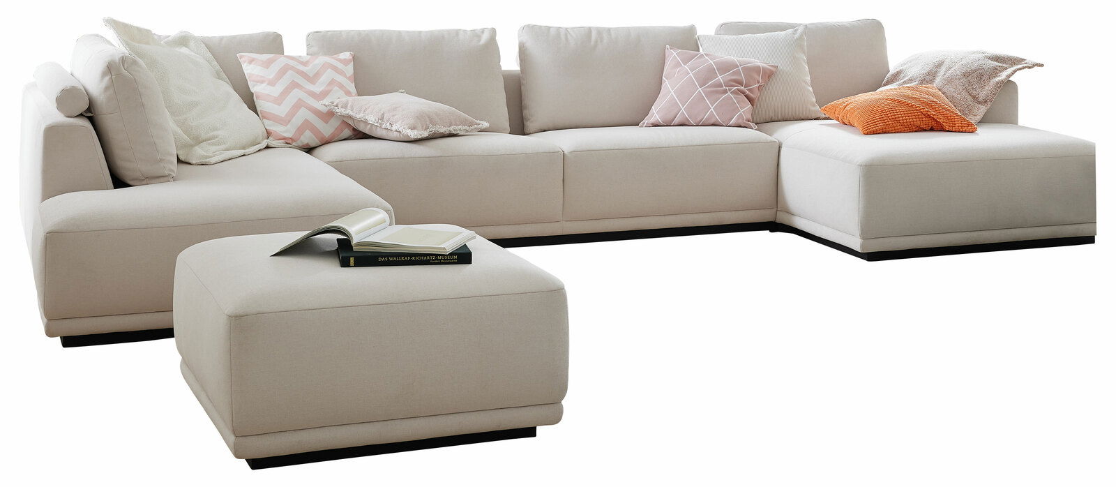 Ecksofa in U-Form mit hellen Polstern und verschiedenen Kissen, aus der Perspektive von vorne links fotografiert.