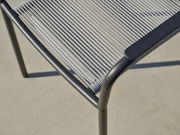 Nahaufnahme eines Stapelsessels mit grauem Metallrahmen und geflochtener Sitzfläche, von oben betrachtet.