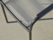 Nahaufnahme eines Stapelsessels mit grauem Metallrahmen und geflochtener Sitzfläche, von oben betrachtet.