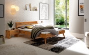 Modernes Schlafzimmer mit einem Kopfteil aus Holz und Metall, seitliche Perspektive. Das Bett ist mit Kissen und einer Decke dekoriert, umgeben von stilvollen Accessoires und einem großen Fenster mit Blick ins Grüne.