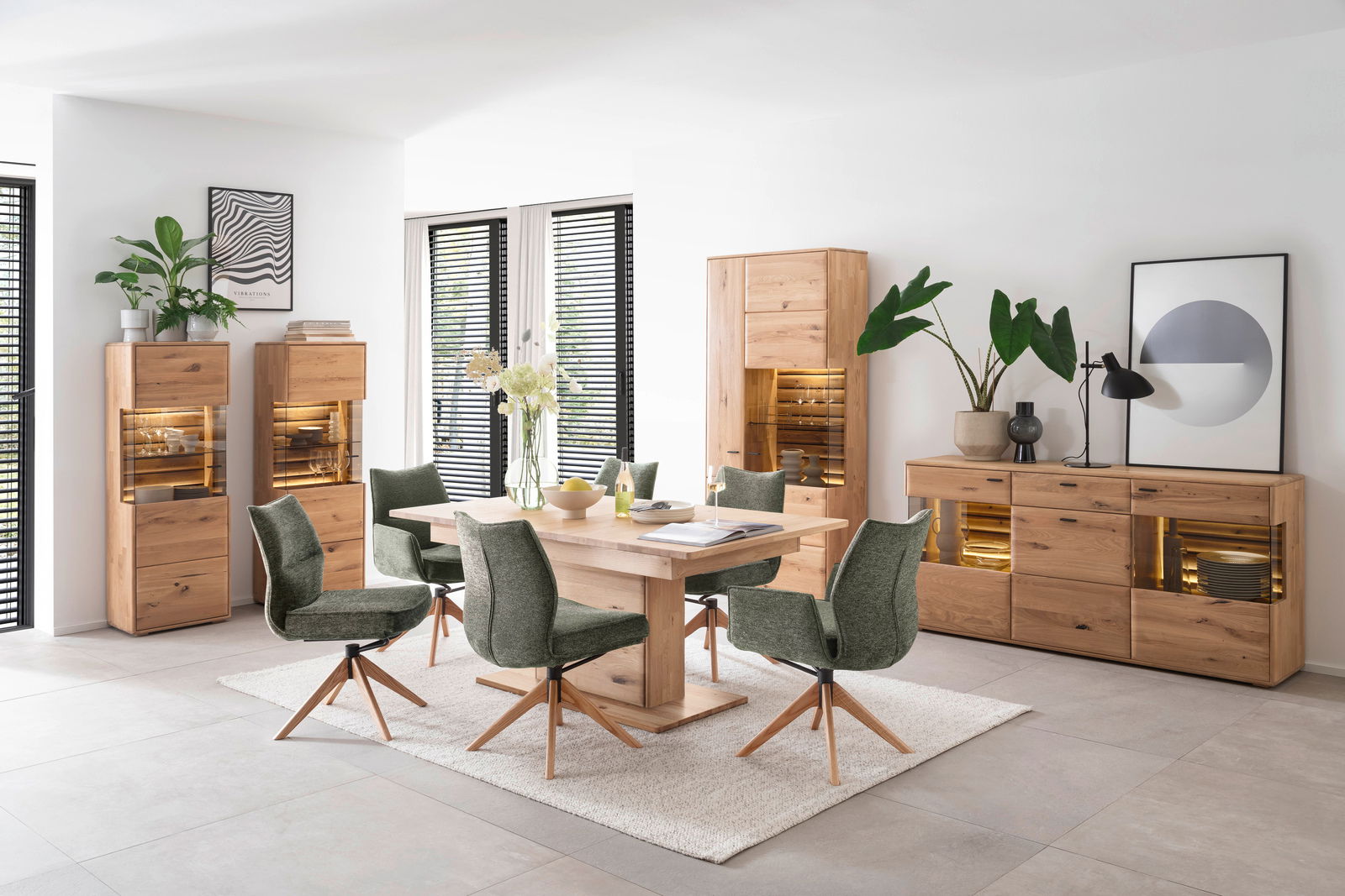 Zurbrüggen Stuhl ASSENTO Esszimmer mit einem Holztisch und grünen Stühlen, umgeben von Holzschränken und Dekorationen, aus der Perspektive des Raumes fotografiert.