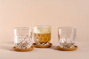 Drei elegante Gläser auf Korkuntersetzern, eines mit Kaffee gefüllt, aus frontaler Perspektive.