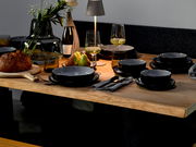 Elegantes Kombiservice 30-tlg. Frost auf einem gedeckten Tisch, seitliche Perspektive, mit modernen schwarzen Tellern und Schalen, umgeben von stilvollen Gläsern, Besteck und Dekoration.