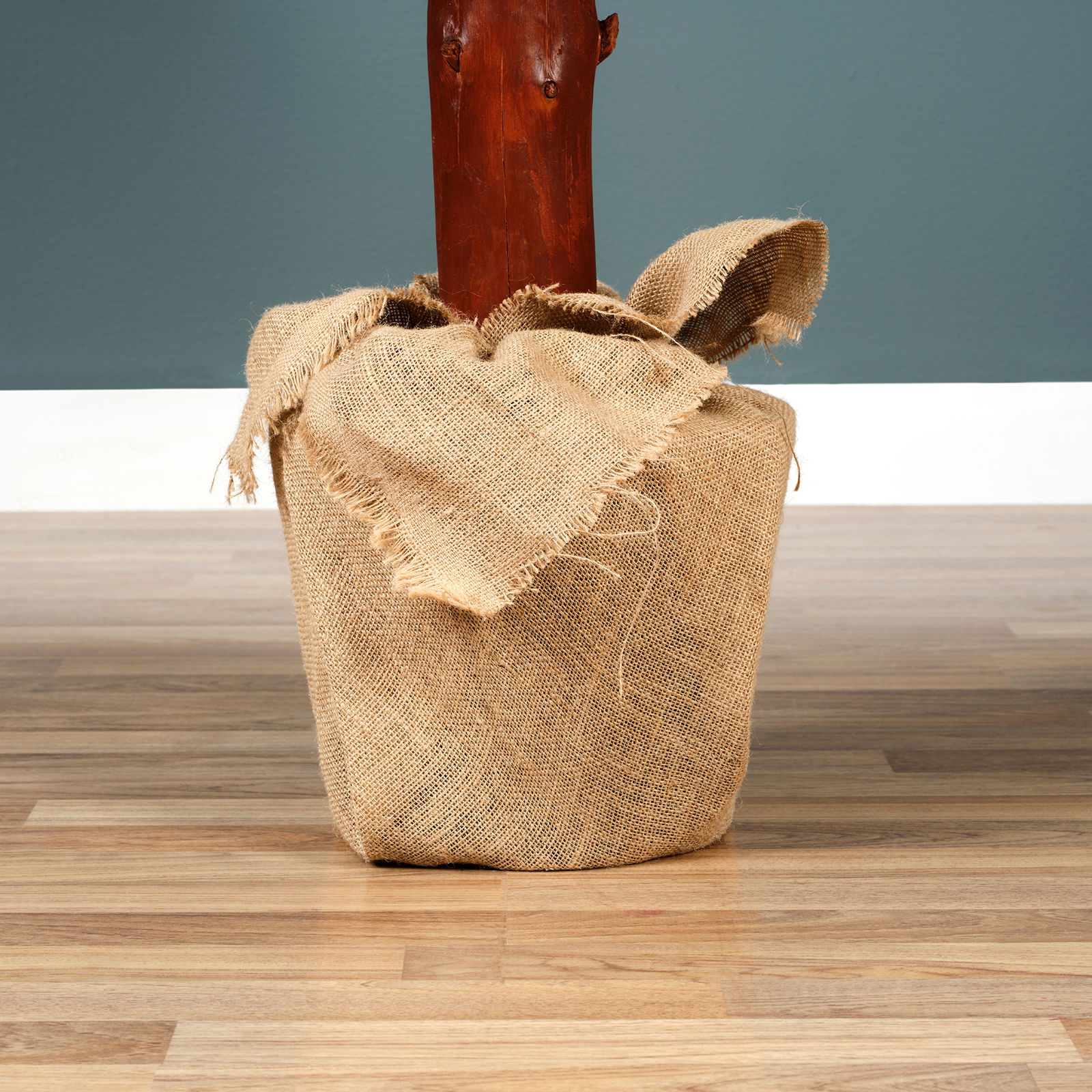 Nahaufnahme eines in Jute eingewickelten Baumstamms auf einem Holzboden vor einer blauen Wand.