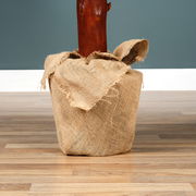 Nahaufnahme eines in Jute eingewickelten Baumstamms auf einem Holzboden vor einer blauen Wand.