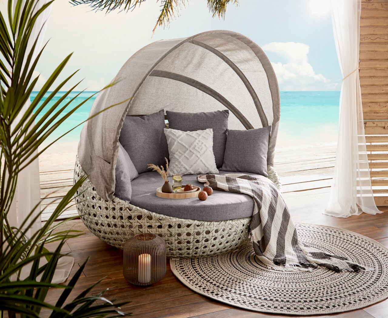Amatio Gartenmuschel DONNA Gartenmuschel mit grauen Kissen und Decke, auf einer Terrasse mit Meerblick, aus seitlicher Perspektive fotografiert.