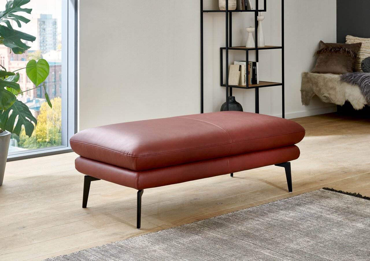 Roter XXL-Hocker aus Leder mit schwarzen Metallbeinen, seitliche Perspektive in modernem Wohnzimmer