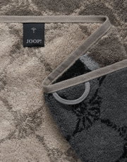 Close-up van een luxe douchehanddoek met een elegant patroon en een JOOP!-label, gefotografeerd vanuit een diagonaal perspectief.