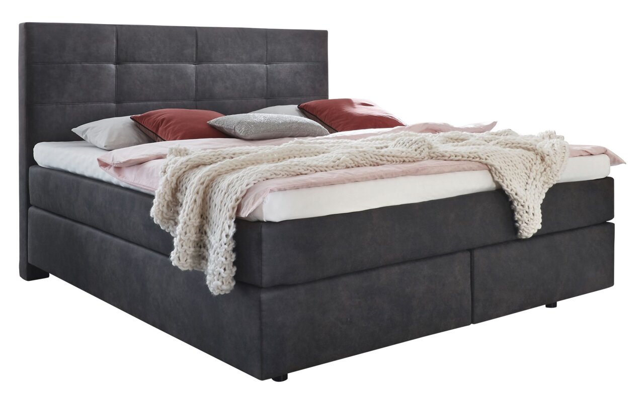 Boxspringbett in dunklem Stoffbezug mit hohem Kopfteil, dekoriert mit Kissen und einer gestrickten Decke, seitliche Perspektive