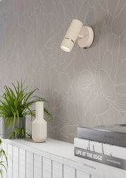 Moderne Wandleuchte CAMINIA in seitlicher Perspektive, montiert an einer stilvollen Wand mit dekorativem Muster, neben einer Pflanze und Büchern.