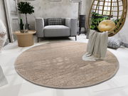 Runder Handweb Teppich in einem modernen Wohnzimmer, umgeben von einem grauen Sofa, einem runden Holztisch und einem hängenden Stuhl mit Kissen. Perspektive von oben.