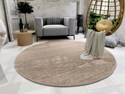 Runder Handweb Teppich in einem modernen Wohnzimmer, umgeben von einem grauen Sofa, einem runden Holztisch und einem hängenden Stuhl mit Kissen. Perspektive von oben.