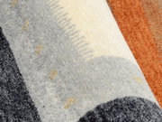 Nahaufnahme eines Wollteppichs mit grauen, weißen und orangefarbenen Streifen. Die Perspektive zeigt eine diagonale Ansicht der Textur.