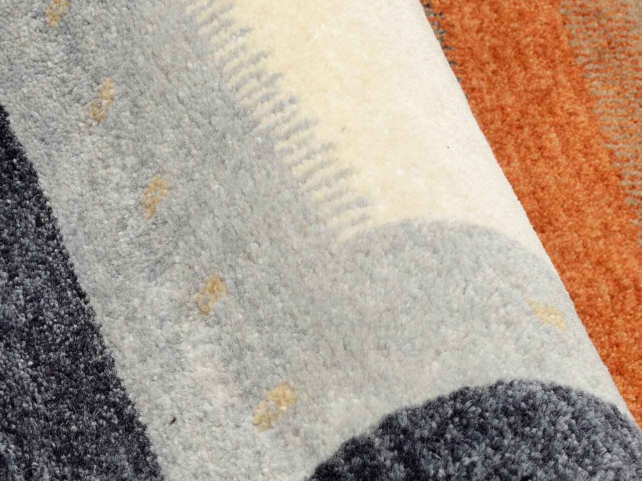 Nahaufnahme eines Wollteppichs mit grauen, weißen und orangefarbenen Streifen. Die Perspektive zeigt eine diagonale Ansicht der Textur.