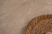 Close-up van een eettafel met een natuurlijke steenlook en een rond, gevlochten placemat van stro, gezien van bovenaf.
