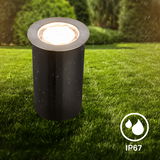 Edelstahl-Bodenleuchte im Freien, zylindrische Form, bei Regen auf einer Rasenfläche, IP67 wasserdicht, seitliche Perspektive