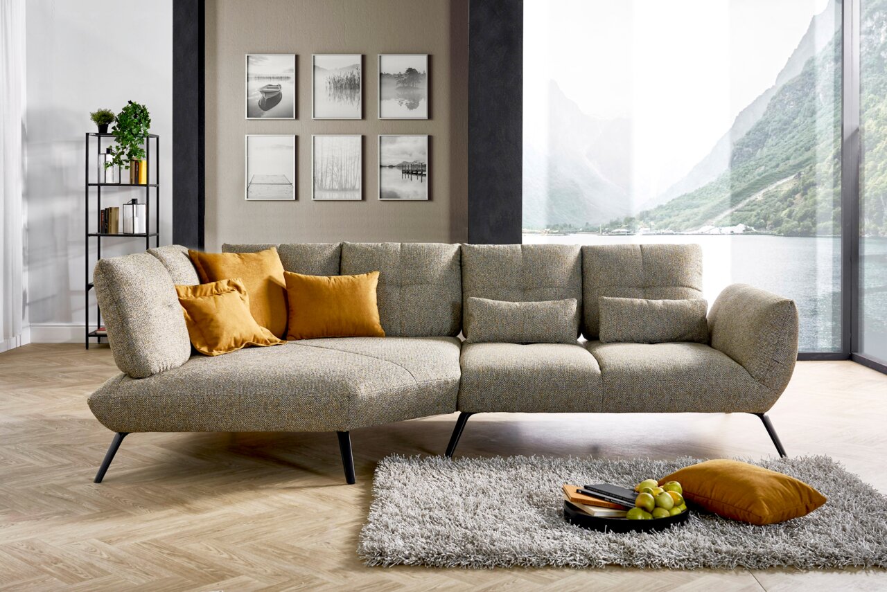 Een moderne zithoek in een stijlvolle woonkamer met uitzicht op een groot raam dat uitkijkt op een schilderachtig landschap. De bank is versierd met gele kussens en staat op een lichte houten vloer naast een zacht tapijt.