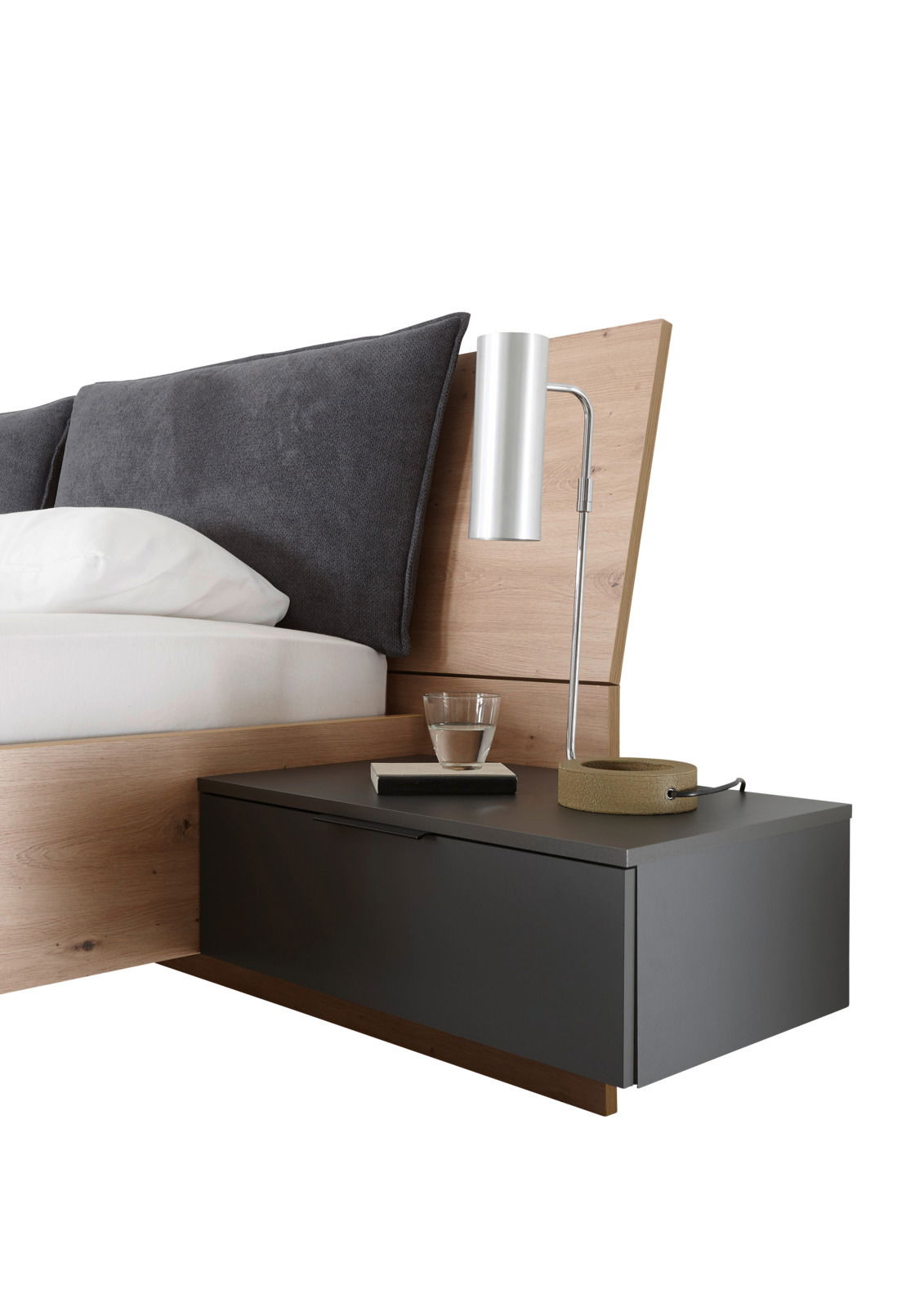 Nahaufnahme einer modernen Bettanlage mit Holz- und Grautönen, inklusive Kopfteil, Kissen, Nachttisch und Lampe von der Seite betrachtet.