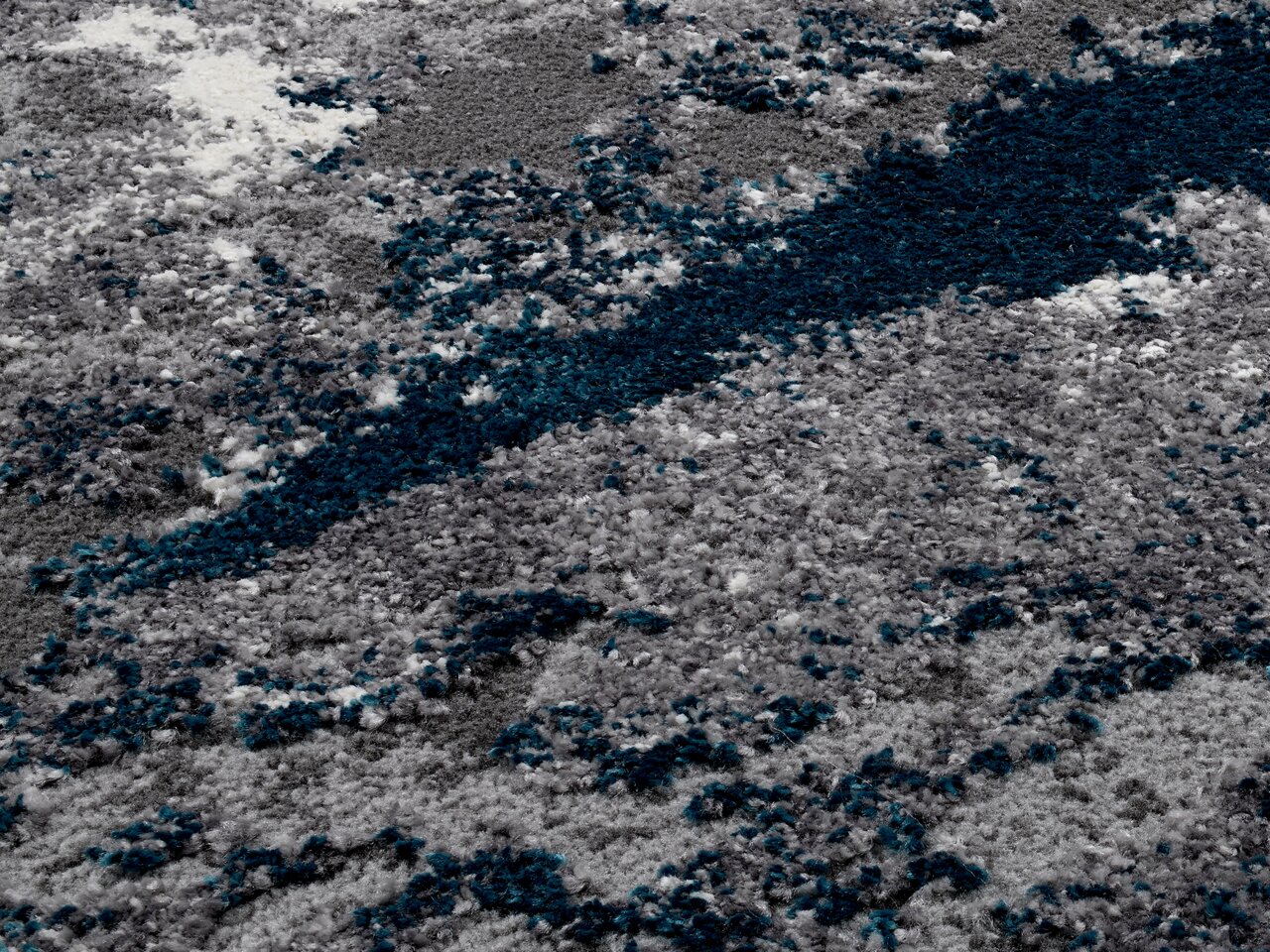 Nahaufnahme eines flauschigen Teppichs in Grau- und Blautönen mit abstraktem Muster.