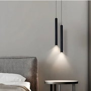 Zwei schlanke schwarze zylindrische Pendelleuchten hängen neben dem Bett und werfen warmes Licht auf eine graue Wand, seitliche Perspektive.