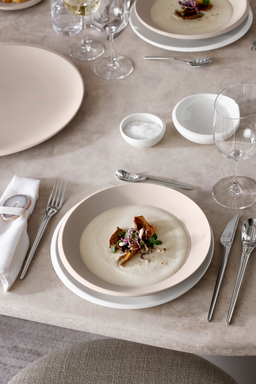 Elegante beige Schale NewMoon 320ml, gefüllt mit einer cremigen Suppe, dekoriert mit Kräutern und Pilzen, auf einem gedeckten Tisch von oben betrachtet.