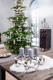 Moderner vierflammiger Kerzenleuchter aus Metall auf einem Tisch mit Lammfellunterlage, im Hintergrund ein Fenster mit winterlicher Aussicht.