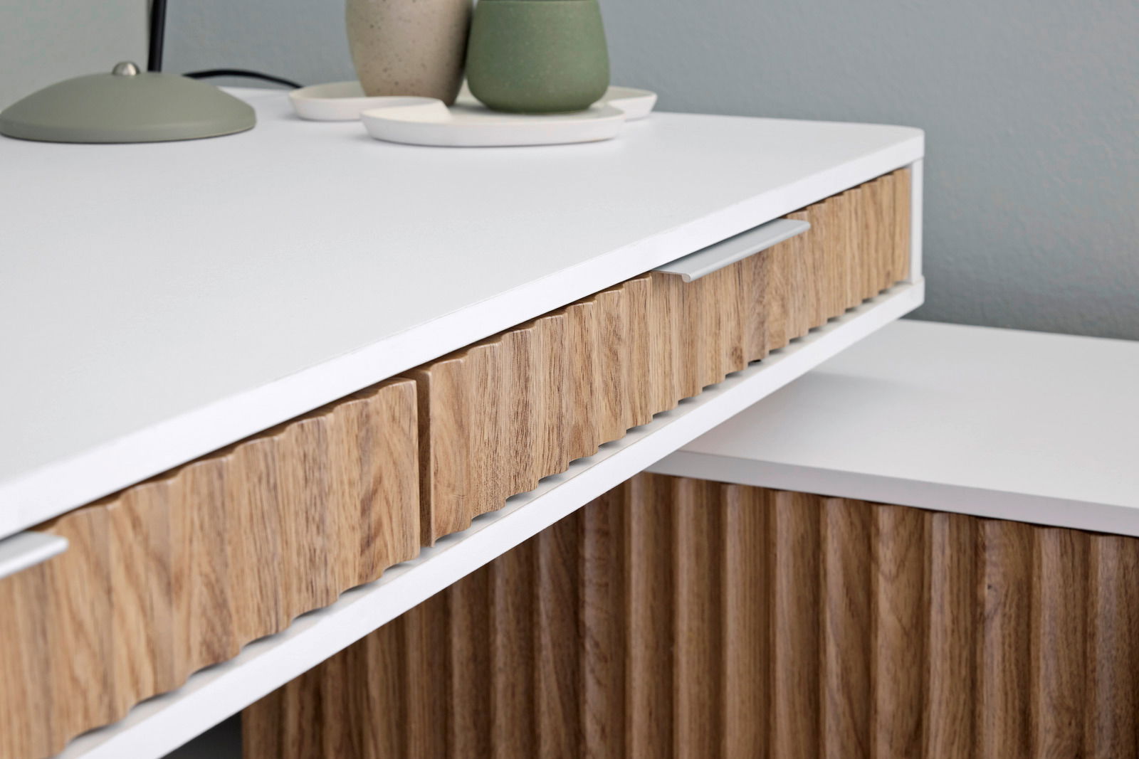 Nahaufnahme eines modernen Eck-Schreibtisches mit weißer Oberfläche und Holzdetails, seitliche Perspektive.