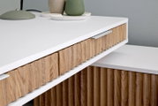 Nahaufnahme eines modernen Eck-Schreibtisches mit weißer Oberfläche und Holzdetails, seitliche Perspektive.