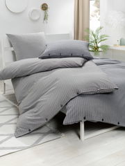 Graue gestreifte Bettwäsche auf einem Bett, seitliche Perspektive mit Kissen und Decke.