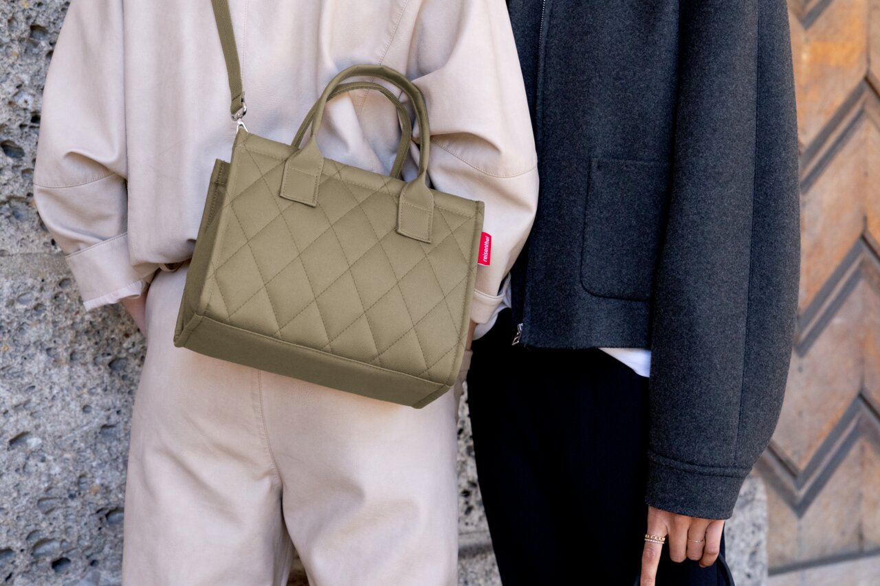 Kleine, olivgrüne Shopper-Tasche mit gestepptem Muster, getragen von einer Person über der Schulter, seitliche Perspektive