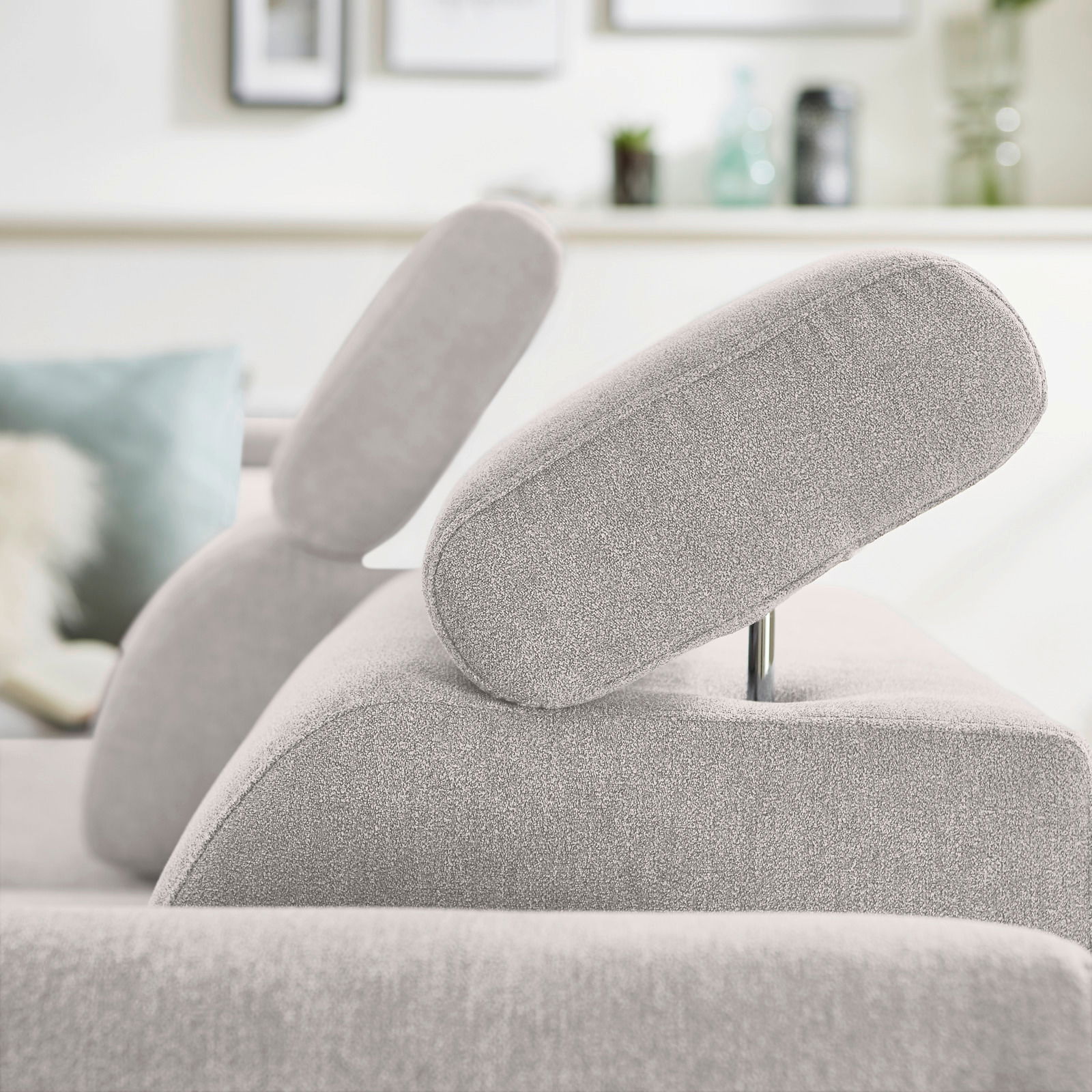 Nahaufnahme eines hellgrauen Ecksofas mit verstellbarer Kopfstütze, seitliche Perspektive.