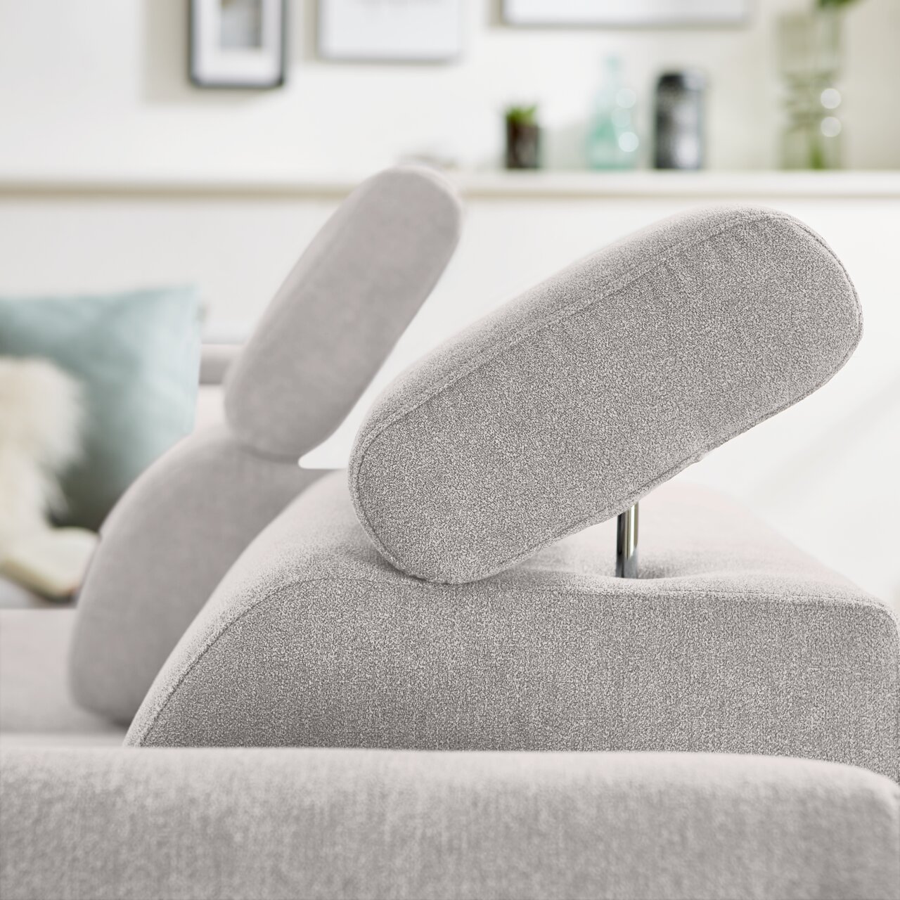 Nahaufnahme eines hellgrauen Ecksofas mit verstellbarer Kopfstütze, seitliche Perspektive.