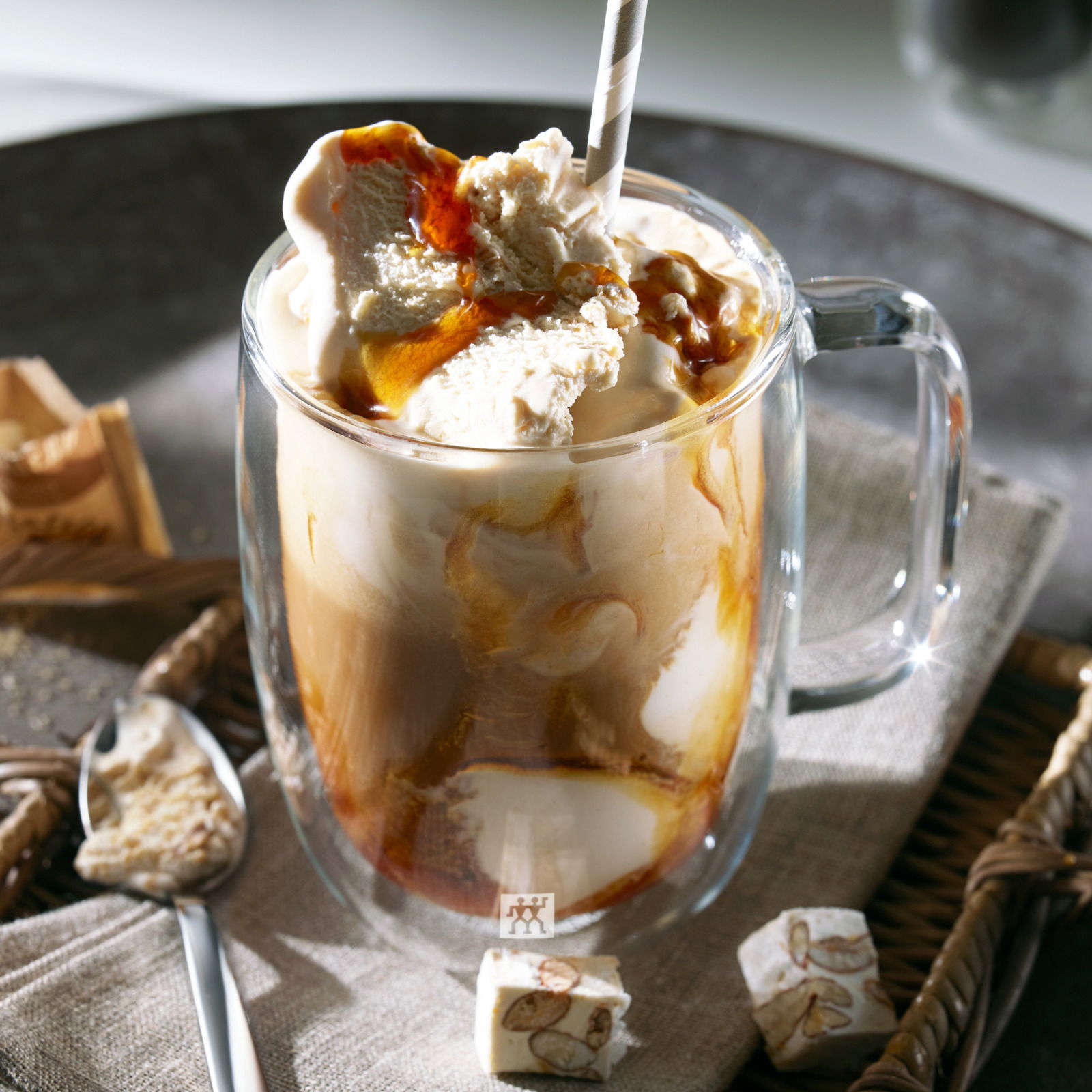 Latte Macchiato in einem doppelwandigen Glas mit Henkel, von schräg oben fotografiert, mit Sahne und Karamellsoße garniert.