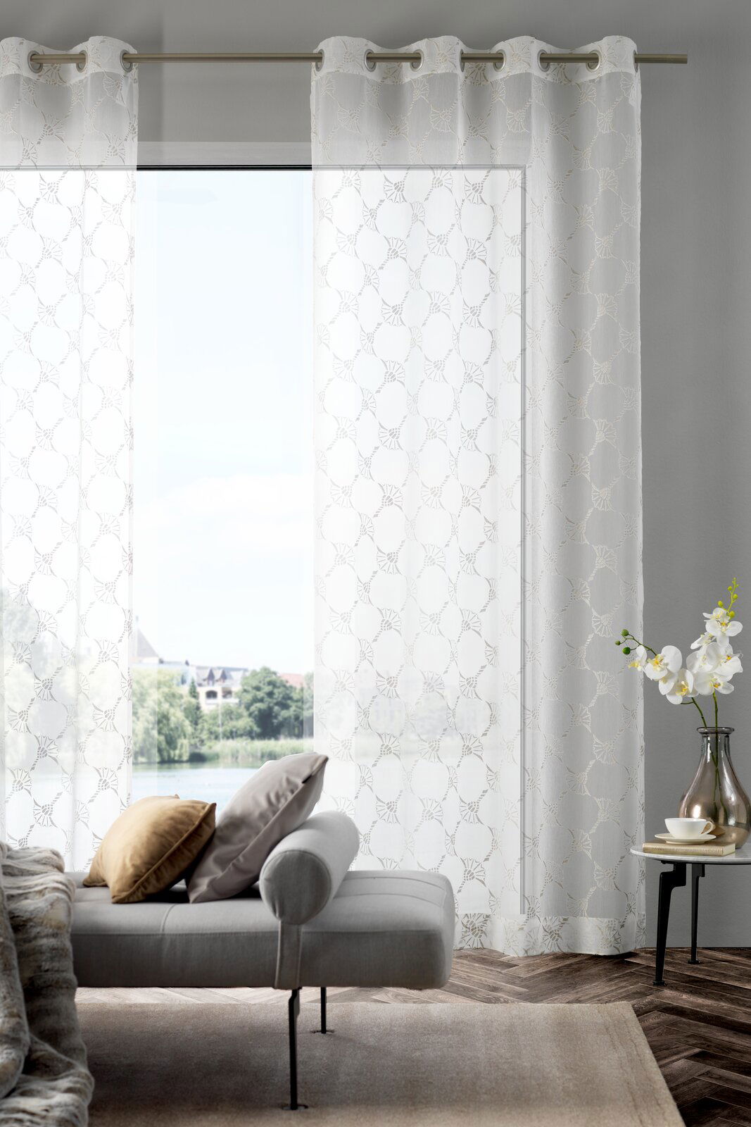 Ösenvorhang J!Airy natur in einem modernen Wohnzimmer, frontal betrachtet, mit einem Sofa und einem Beistelltisch im Vordergrund.