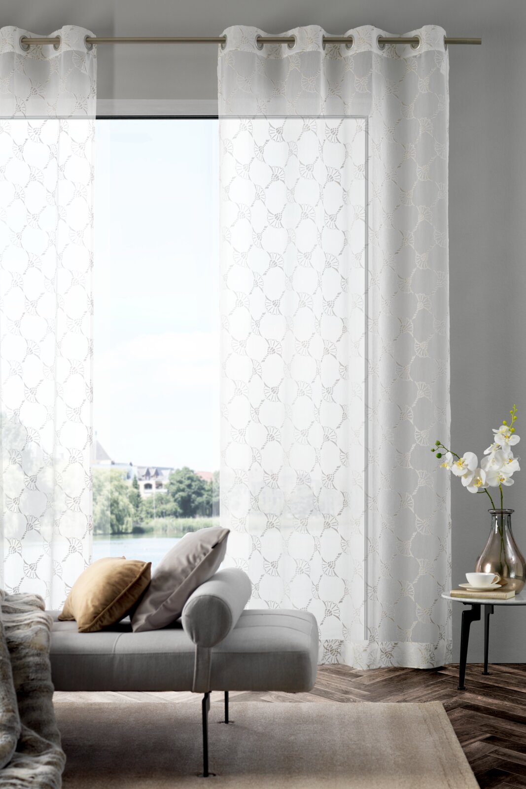 Ösenvorhang J!Airy natur in einem modernen Wohnzimmer, frontal betrachtet, mit einem Sofa und einem Beistelltisch im Vordergrund.