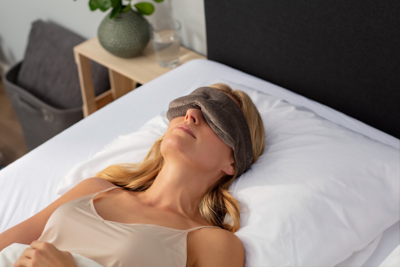 Frau liegt entspannt auf einem Bett und trägt eine Tempur Schlafmaske, seitliche Perspektive