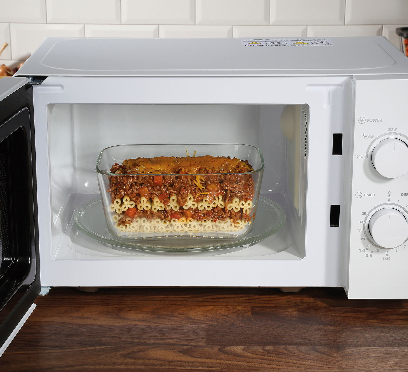 Mikrowelle mit geöffneter Tür, darin eine Glasauflaufform mit Nudelauflauf, seitliche Perspektive