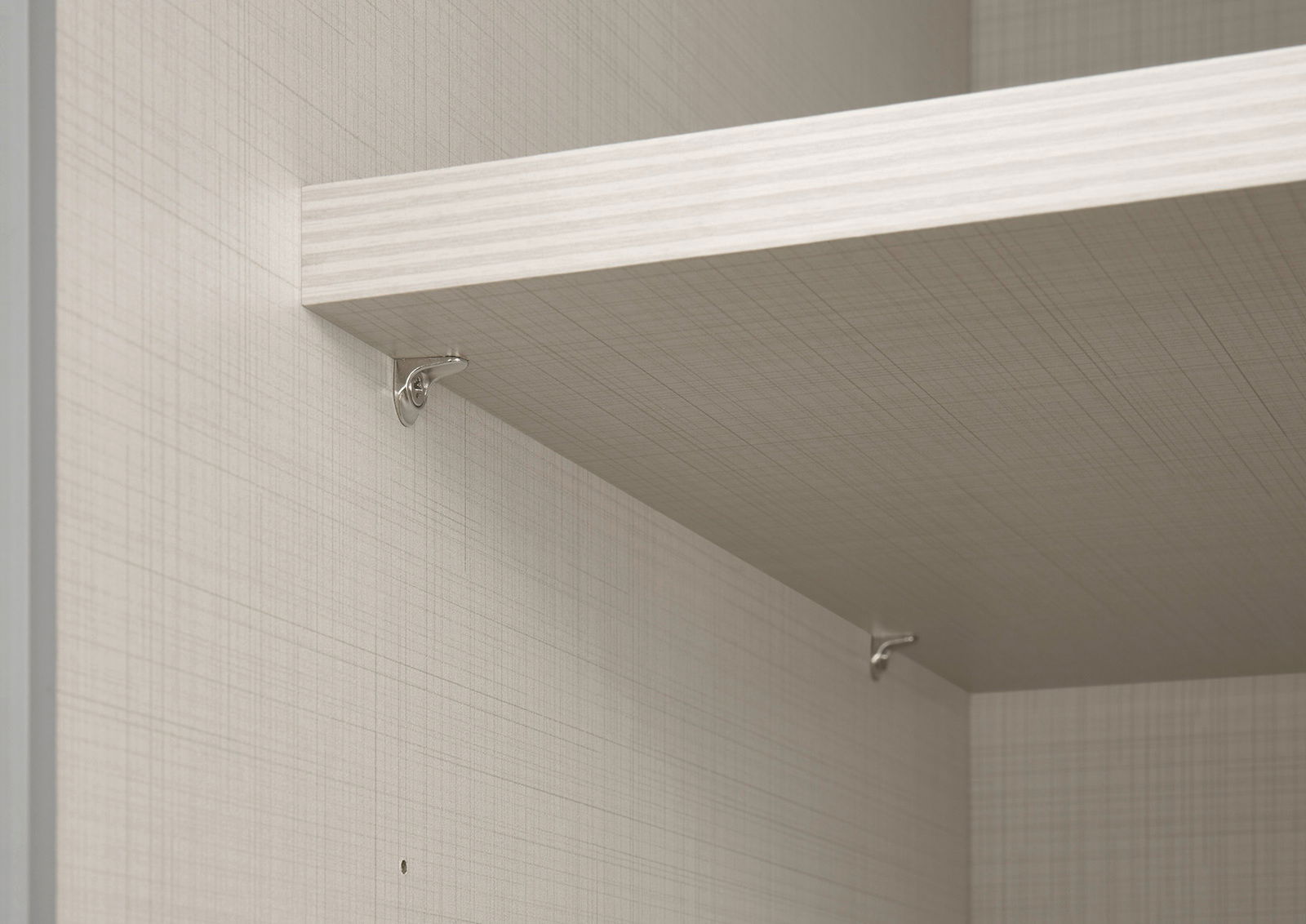 Nahaufnahme eines Einlegebodens in einem Schwebetürenschrank, montiert mit Metallhalterungen. Perspektive von unten links.