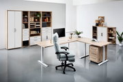 Moderne Büroumgebung mit L-förmigem Schreibtisch, ergonomischem Bürostuhl und Regalsystemen in Holzoptik, aus der Perspektive von vorne rechts betrachtet.