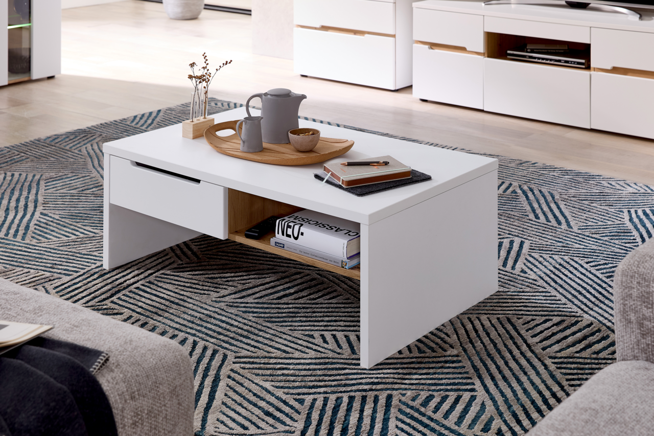 Moderner weißer Couchtisch mit Schublade und Ablagefach, dekoriert mit Tablett und Accessoires, aus seitlicher Perspektive fotografiert.