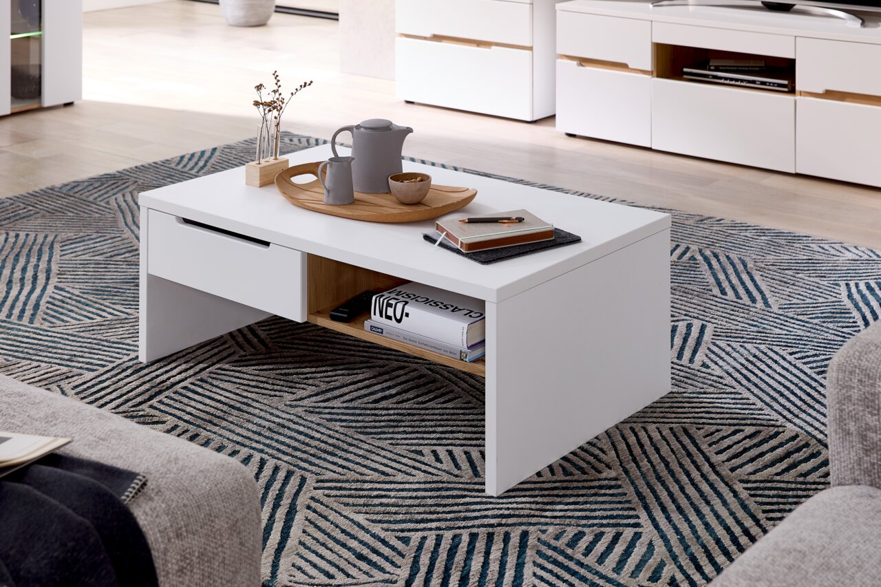 Moderner weißer Couchtisch mit Schublade und Ablagefach, dekoriert mit Tablett und Accessoires, aus seitlicher Perspektive fotografiert.