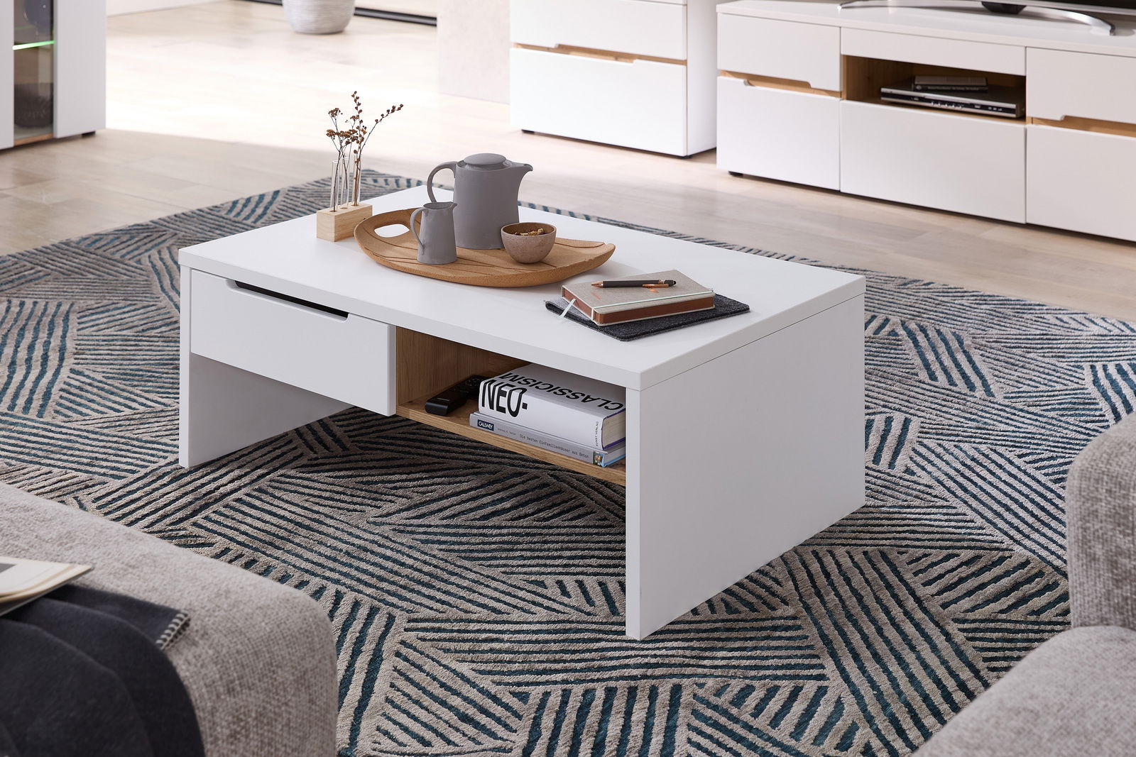 Moderner weißer Couchtisch mit Schublade und Ablagefach, dekoriert mit Tablett und Accessoires, aus seitlicher Perspektive fotografiert.