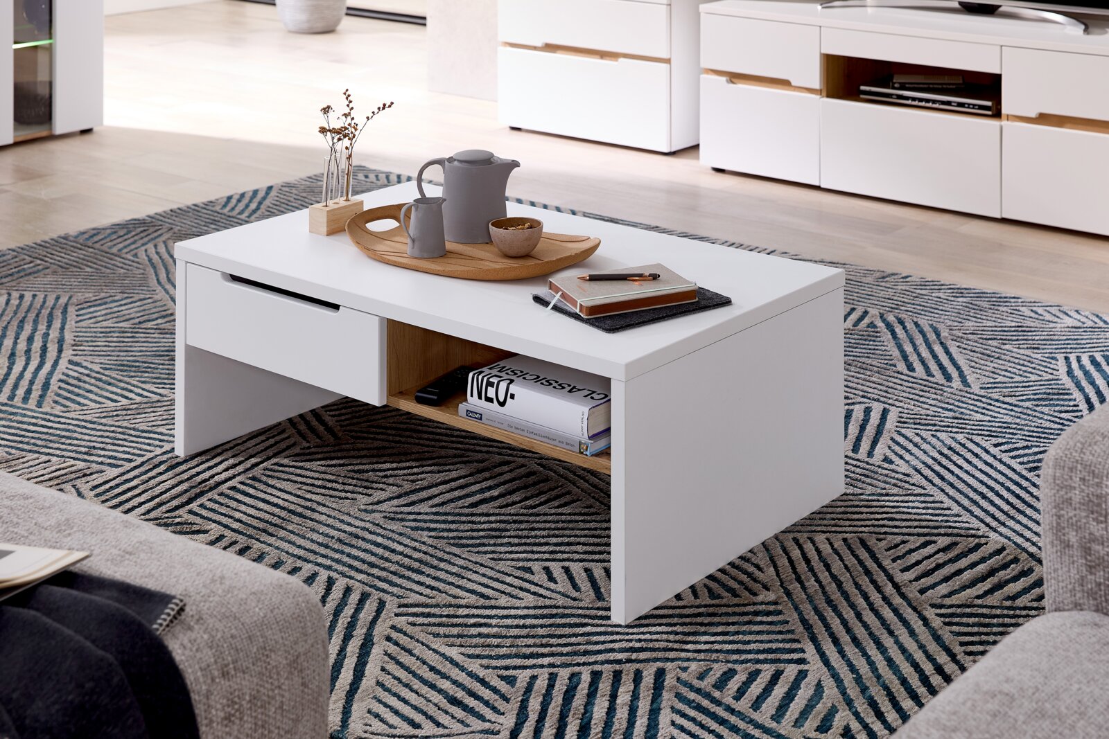 Moderner weißer Couchtisch mit Schublade und Ablagefach, dekoriert mit Tablett und Accessoires, aus seitlicher Perspektive fotografiert.
